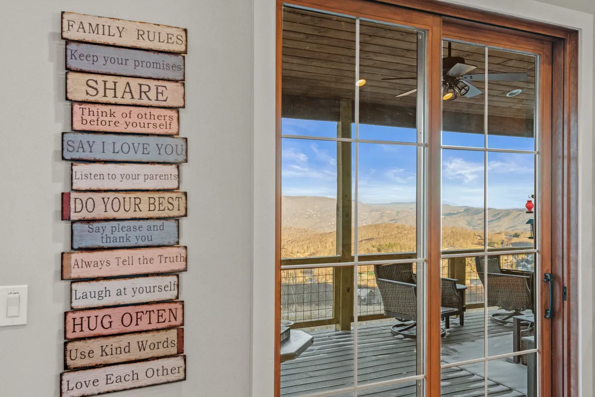 Interior view featuring a 'family rules' sign, glass doors that open to a deck, and a stunning mountain vista beyond. The inviting space encourages moments of reflection or remote work while staying connected to the natural world outside.
