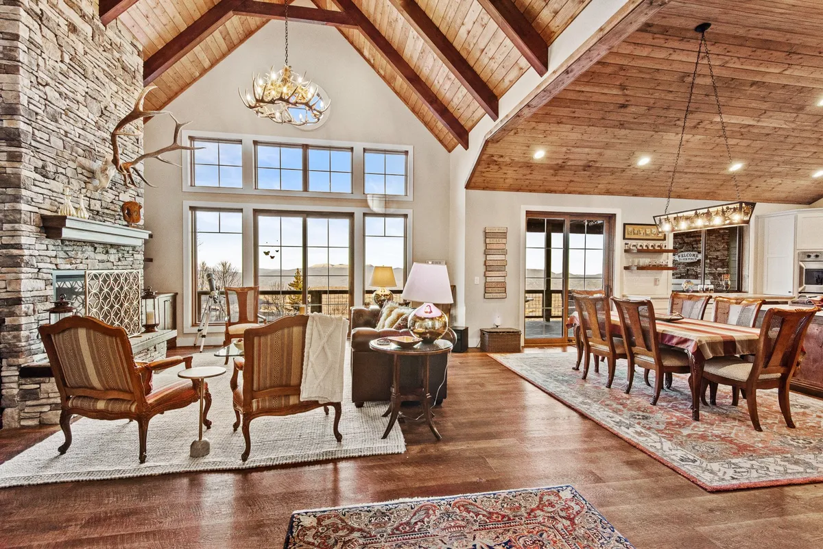A beautifully appointed living and dining area featuring a large stone fireplace, high wooden ceiling, and a comfortable seating arrangement. The dining table is visible, and the room’s design encourages both family gatherings and intimate conversations.