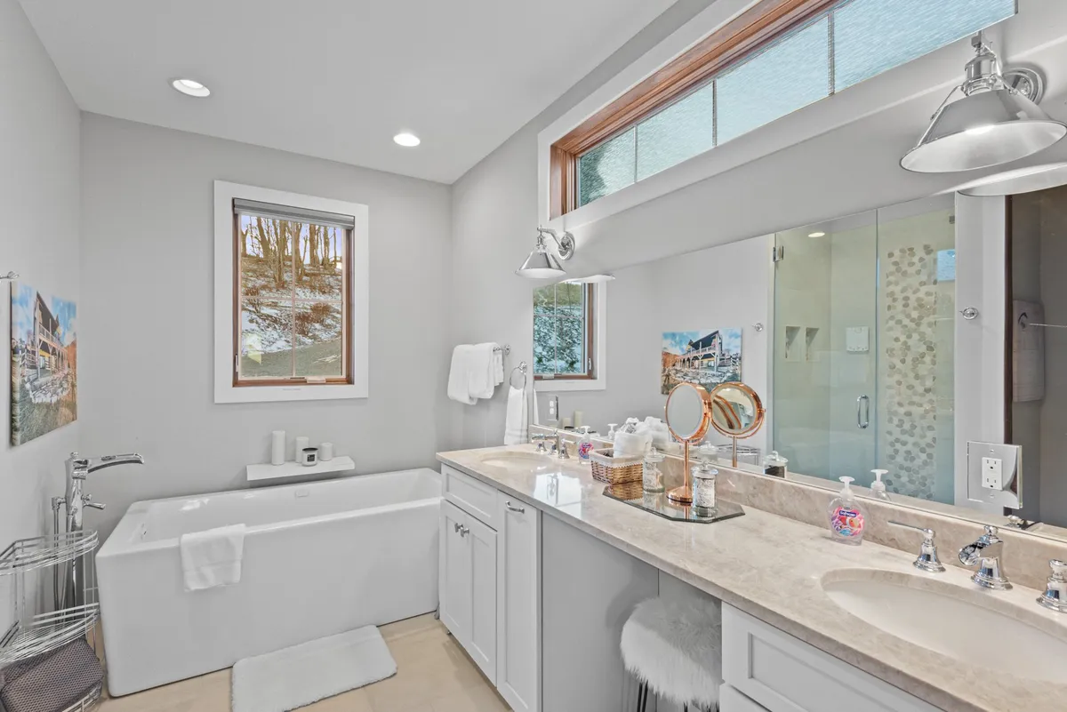 A luxurious ensuite bathroom featuring a bathtub, double vanity with a large mirror, shower area, and a window letting in natural light. The space is modern and inviting, ideal for unwinding after a day of adventure.