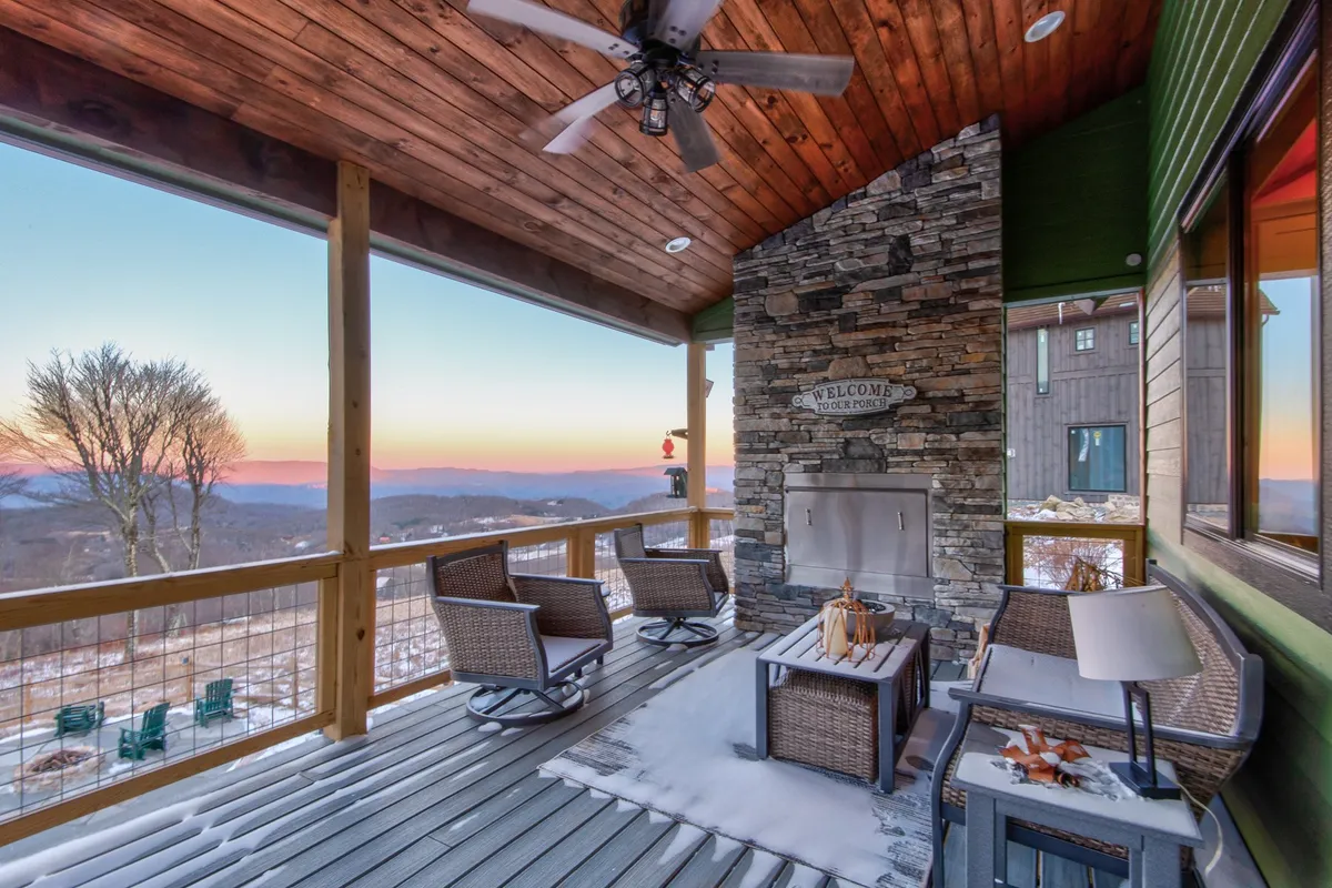 The image features a stone fireplace outdoors, surrounded by a cozy sitting area with wicker chairs and a panoramic mountain view. The inviting space is ideal for enjoying the warmth of a fire while taking in the surrounding beauty, especially at sunset.