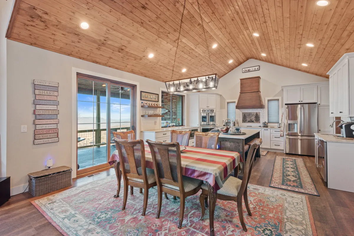 A bright, open dining area with a striped tablecloth on the dining table, a modern kitchen island, and large windows offering scenic views. The proximity of the kitchen and dining area fosters a sense of togetherness, while the setting feels festive and welcoming.