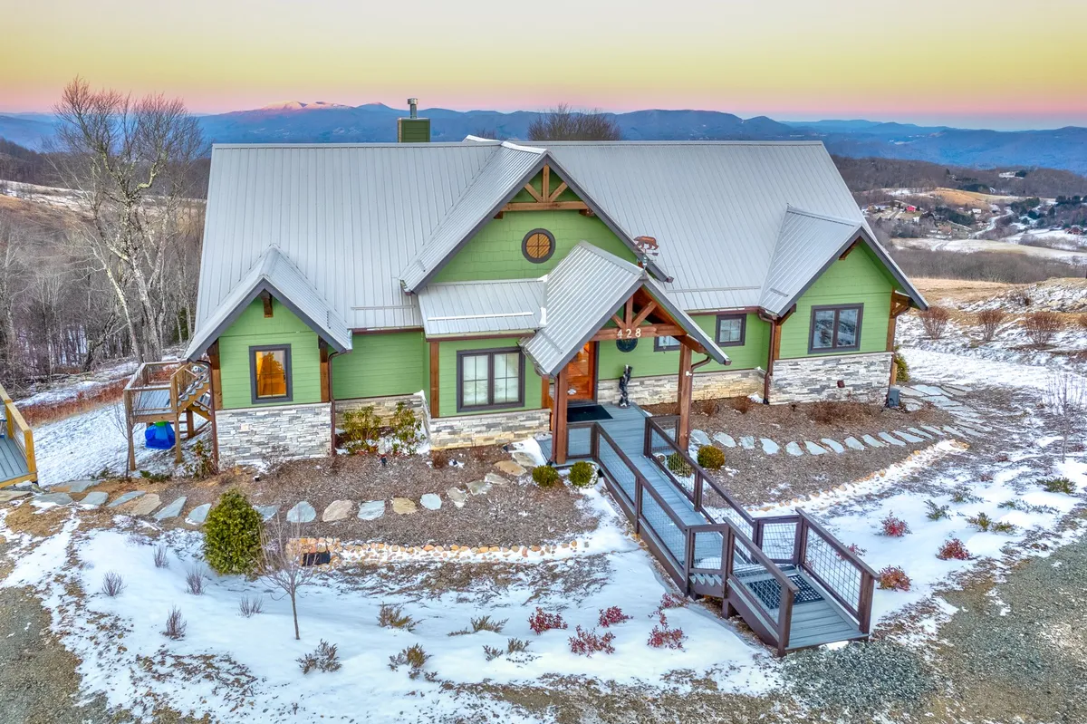 The image presents the home’s green facade, a charming stone pathway leading to the entrance, and a snow-covered landscape framed by distant mountain views. The scene is peaceful and encapsulates the rural, secluded feel mentioned in the section.