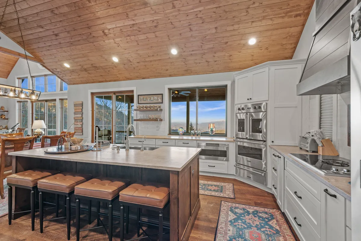 A spacious kitchen with a large island, panoramic windows, modern appliances, and a wooden ceiling. The kitchen is designed for both practicality and style, perfect for family cooking sessions or entertaining guests while enjoying mountain vistas.