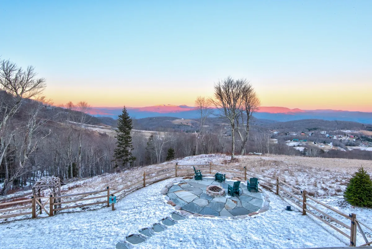 This photo shows a stone fire pit with green chairs arranged on a snow-covered ground, set against a backdrop of mountain views. The spacious yard is ideal for pets to play safely while their owners enjoy the scenery or gather for socializing.
