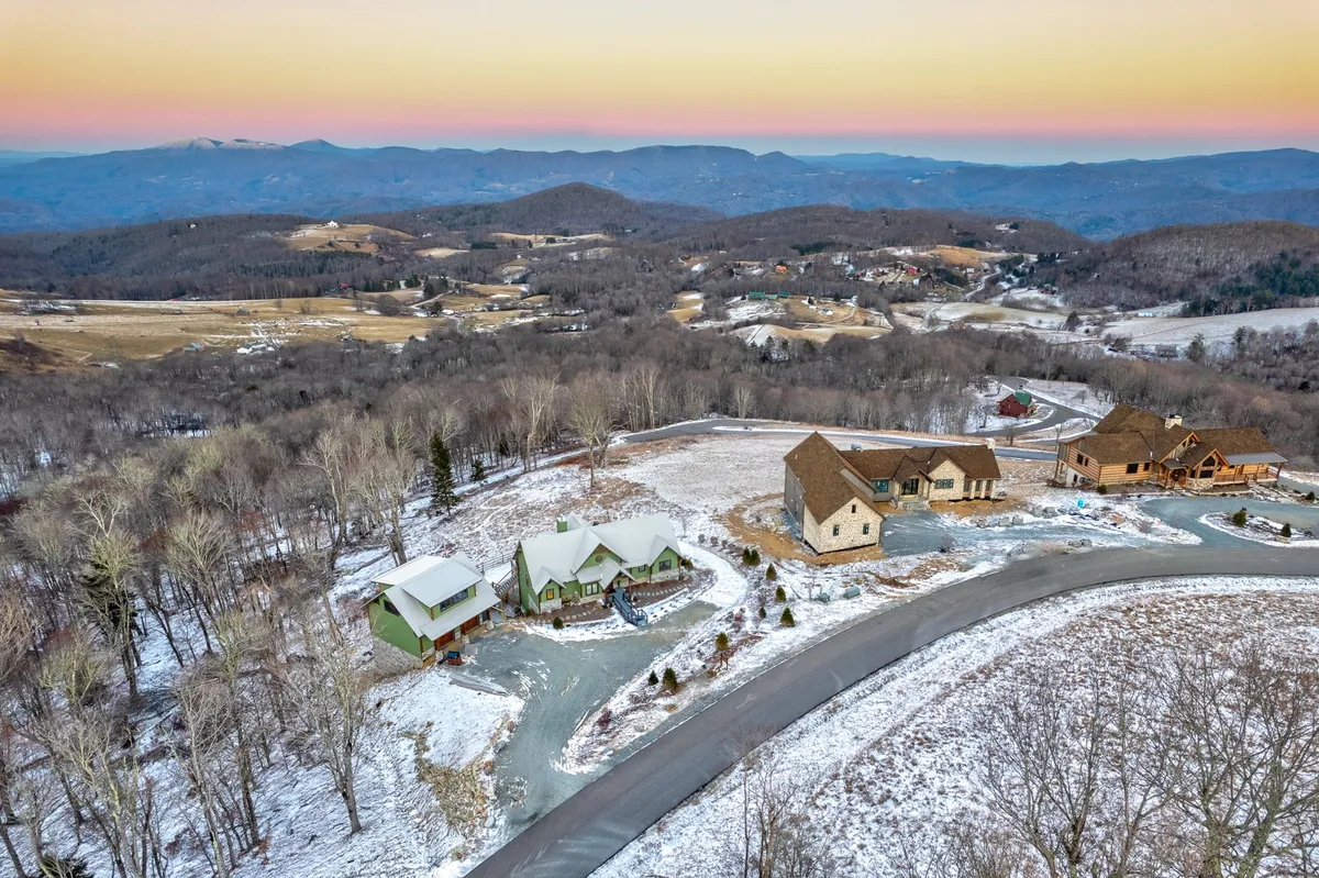A sweeping view of the mountainous landscape with a snow-covered ground, scattered cabins, and a winding road. The image captures the vastness and serenity of the Blue Ridge setting, inviting families to imagine hiking, wildlife spotting, or setting out for a day of skiing or tubing.