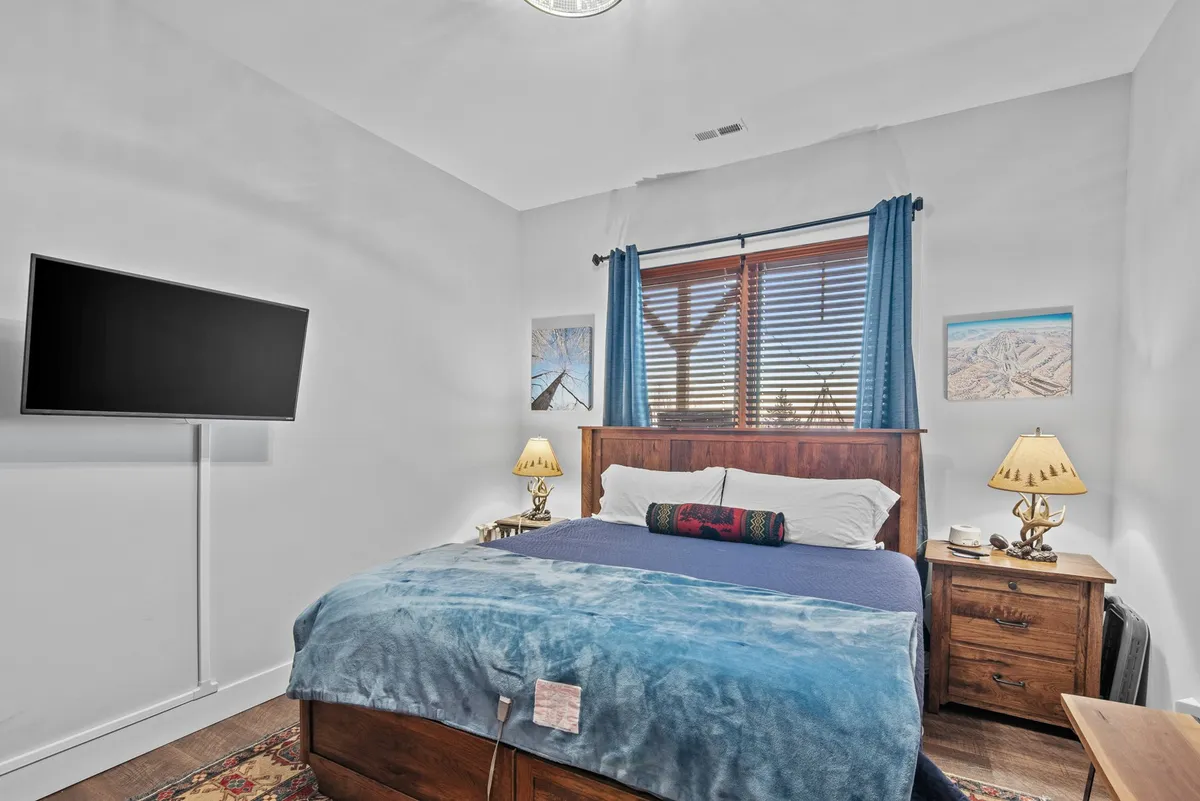 A restful king bedroom scene with a bed, Smart TV, nightstands, curtains, and tasteful artwork. The space feels inviting and private, offering a cozy spot to relax or watch TV in comfort.