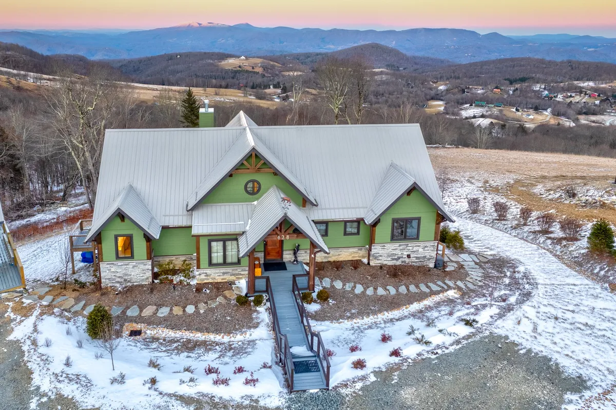 The image showcases the striking exterior of Sunbird Cabin, nestled among rolling mountains with a welcoming pathway leading to the entrance. The house is framed by panoramic views of the Blue Ridge Mountains, hinting at the opportunity for outdoor gatherings, hiking adventures, and peaceful moments on the porch while watching the sunrise or enjoying snowfall in winter.
