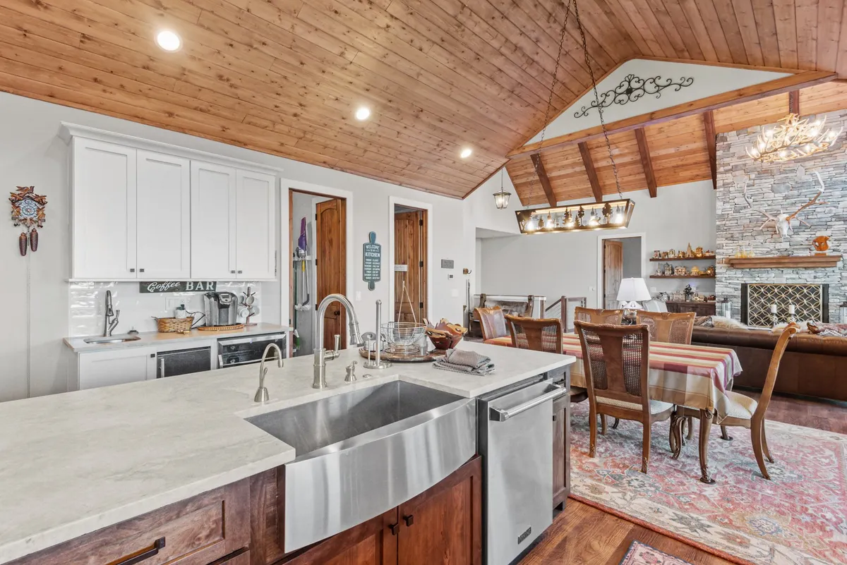 A warm, inviting open-plan space with a kitchen island, dining area, stone fireplace, exposed wooden beams, and decorative touches. The layout encourages seamless flow between cooking, dining, and relaxing, with a focus on togetherness.